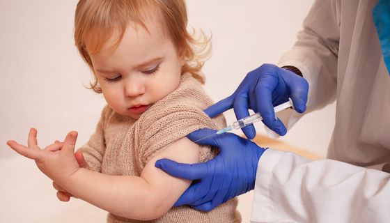 Medizinisches Fachpersonal impft ein Kleinkind. Es schaut kritisch.