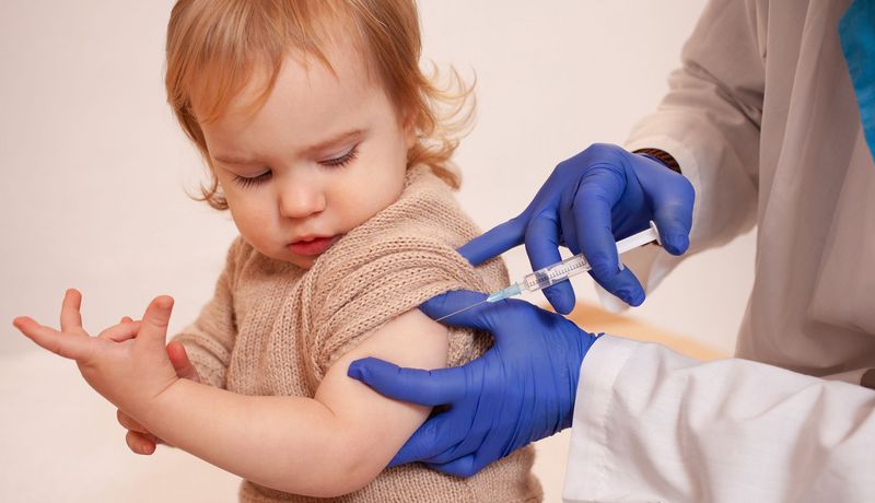 Medizinisches Fachpersonal impft ein Kleinkind. Es schaut kritisch.