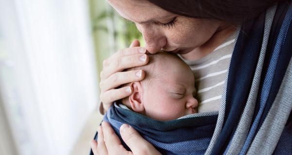 Mutter, hat ihr Baby in einer Trage und küsst es auf den Kopf.