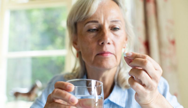 Eine ältere Frau hält ein Glas Wasser und eine Tablette in den Händen.