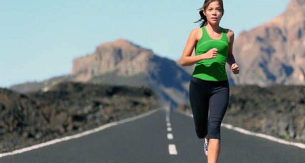 Junge Frau läuft auf einer Straße in menschenleerer Landschaft.