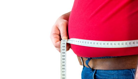 Mann mit rotem Shirt legt ein Maßband um seinen dicken Bauch