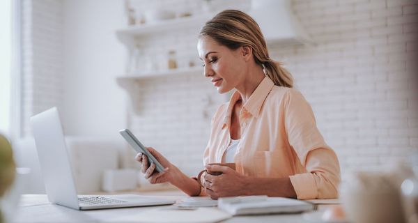 Junge Frau, sitzt am Schreibtisch, schaut auf ihr Smartphone.