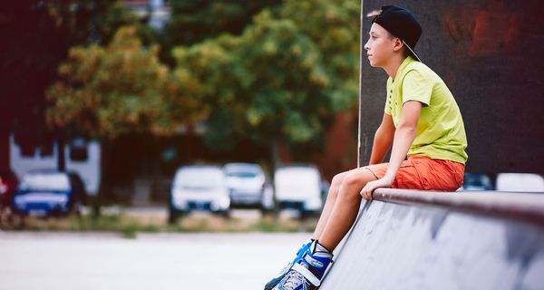 Jugendlicher mit Inline-Skates, sitzt auf einer Skatebahn.