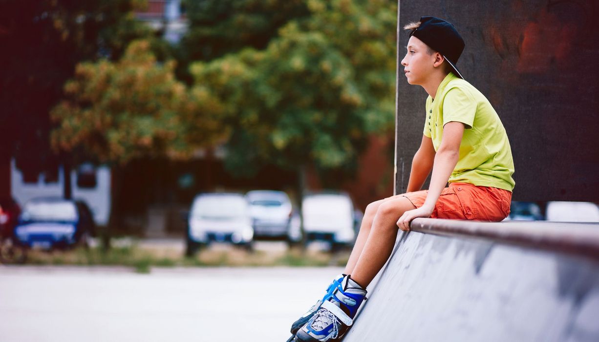 Jugendlicher mit Inline-Skates, sitzt auf einer Skatebahn.