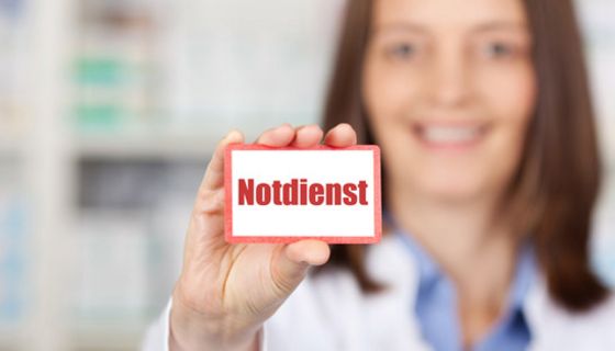 Apothekerin hält Schild in die Kamera, auf dem "Notdienst" steht