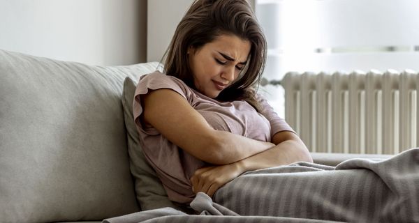 Junge Frau mit Bauchschmerzen, liegt im Bett.