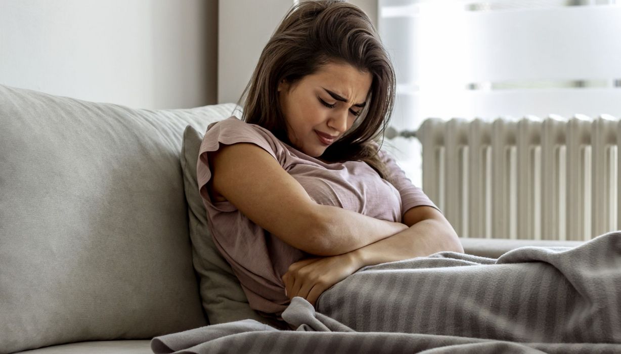 Junge Frau mit Bauchschmerzen, liegt im Bett.