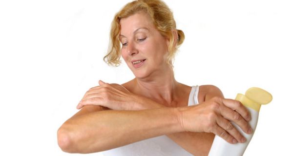 Frau mittleren Alters in weißem Trägershirt cremt sich den rechten Oberarm ein