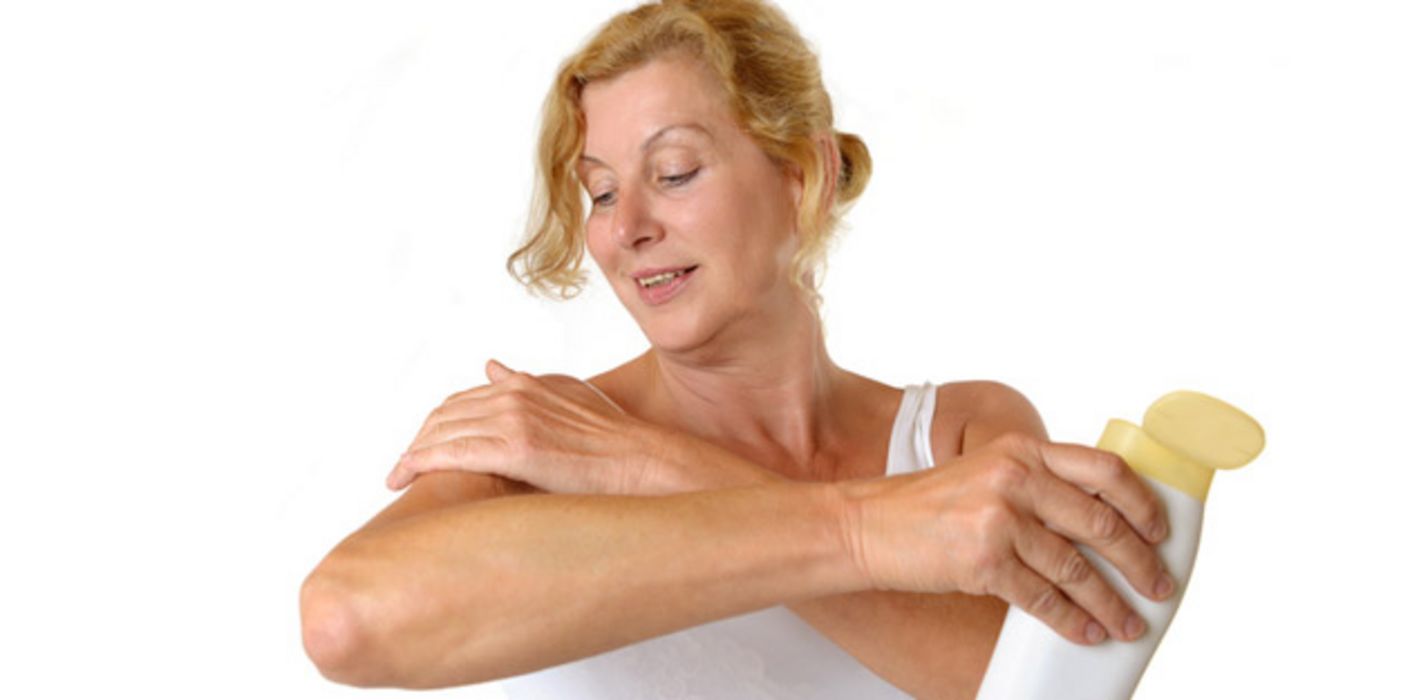 Frau mittleren Alters in weißem Trägershirt cremt sich den rechten Oberarm ein