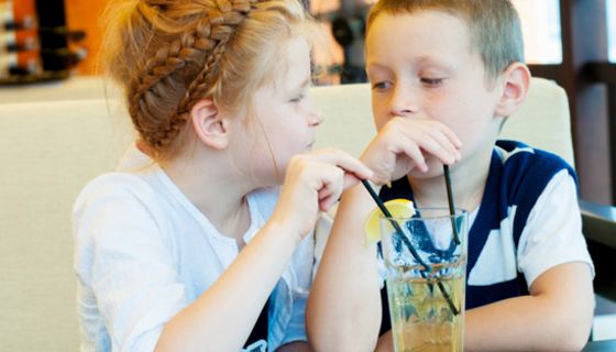 Mädchen und Junge, ca. 6 Jahre, trinken am Tisch gemeinsam aus Limoglas mit Strohhalm