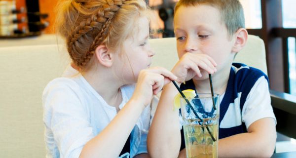 Mädchen und Junge, ca. 6 Jahre, trinken am Tisch gemeinsam aus Limoglas mit Strohhalm