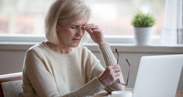 Ältere Frau, sitzt vor dem Laptop und greift sich an die Augen.