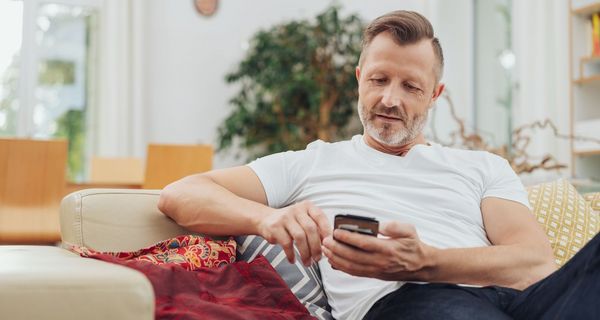 Älterer Mann, mit Smartphone auf der Couch.