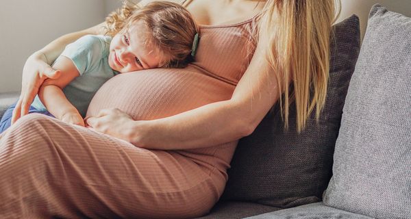 Junge schwangere Frau, kuschelt mit ihrer kleinen Tochter.