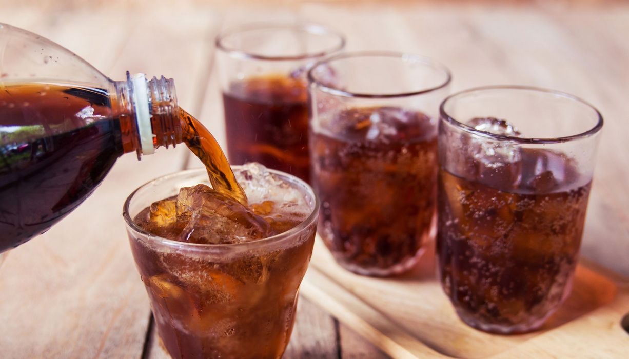 Cola wird aus einer Flasche in kleine Gläser eingeschenkt.