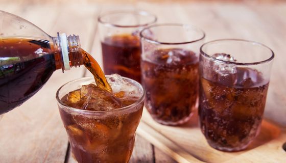 Cola wird aus einer Flasche in kleine Gläser eingeschenkt.