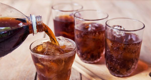 Cola wird aus einer Flasche in kleine Gläser eingeschenkt.