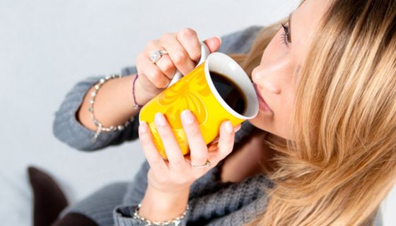 Frau trinkt Kaffee aus gelber Tasse.