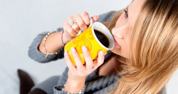 Frau trinkt Kaffee aus gelber Tasse.