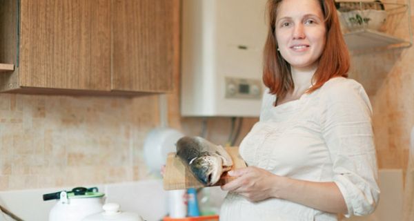 Schwangere steht mit einem Lachs in der Küche