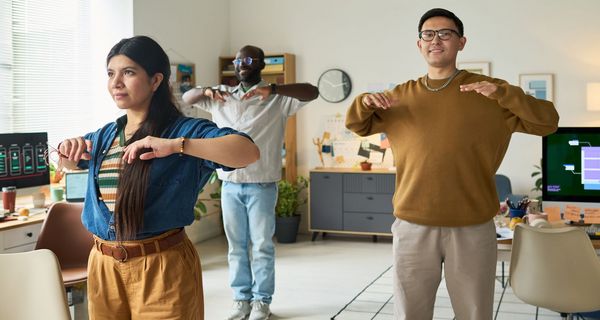 Eine Frau und zwei Männer machen einfache Fitnessübungen im Großraumbüro.