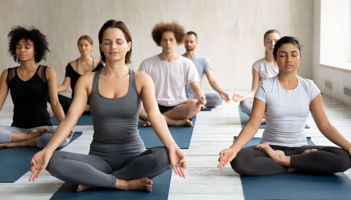 Eine Gruppe junger Frauen und Männer meditiert in einem Gruppenraum.