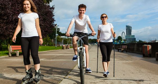 Drei junge Leute fahren Inline-Skates, fahren Fahrrad und machen Nordic Walking