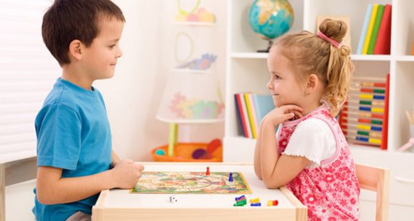 Mädchen und Junge sitzen am Tisch und spielen ein Brettspiel.