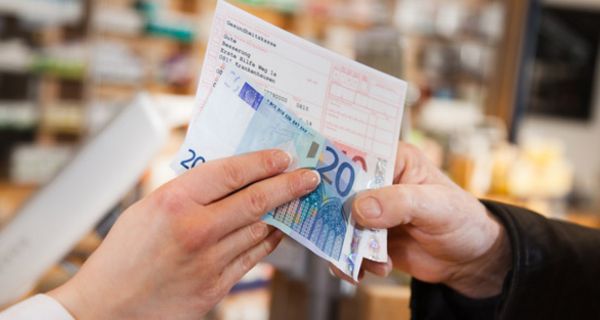 Szene in einer Apotheke: Zwei Hände an einem Rezept und einem 20-Euro-Schein