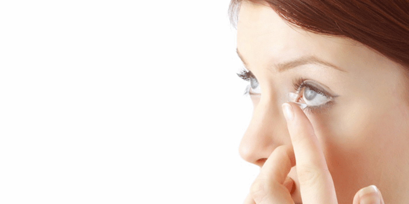 Eine Frau, rote Haare, setzt sich eine Kontaktlinse ins Auge. 