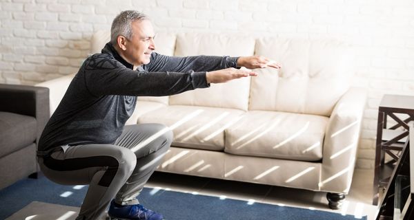 Mann macht Kniebeugen zu Hause im Wohnzimmer