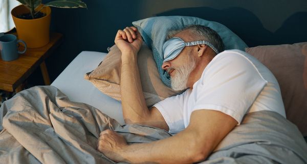 Älterer Herr schläft mit einer seidenen Schlafmaske auf der Seite.