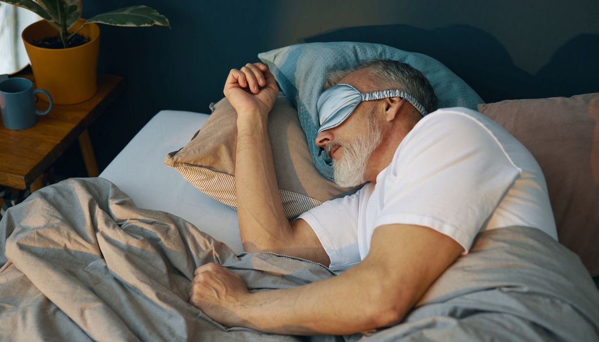Älterer Herr schläft mit einer seidenen Schlafmaske auf der Seite.