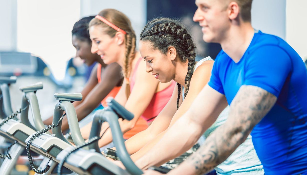 Drei Frauen und ein Mann machen in einem Fitnessstudio nebeneinander Ausdauersport.