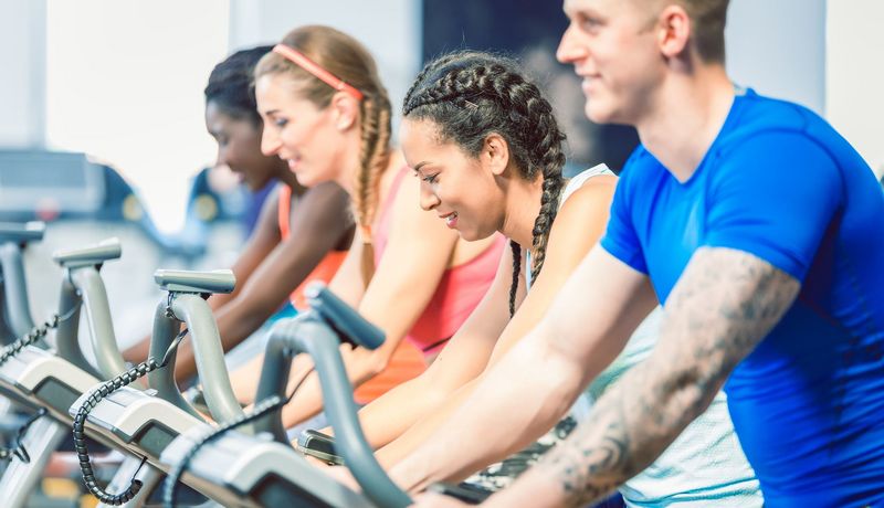 Drei Frauen und ein Mann machen in einem Fitnessstudio nebeneinander Ausdauersport.