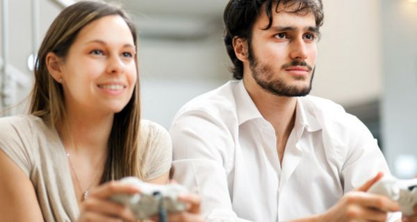 Junge Frau und junger Mann sitzen nebeneinander und halten Spielkonsolen in der Hand
