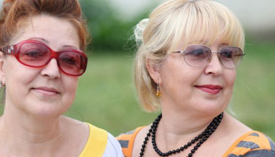 Frauen, verschieden gekleidete Zwillinge, ca. Mitte 50, bunte Freizeitkleidung, schauen in die Kamera