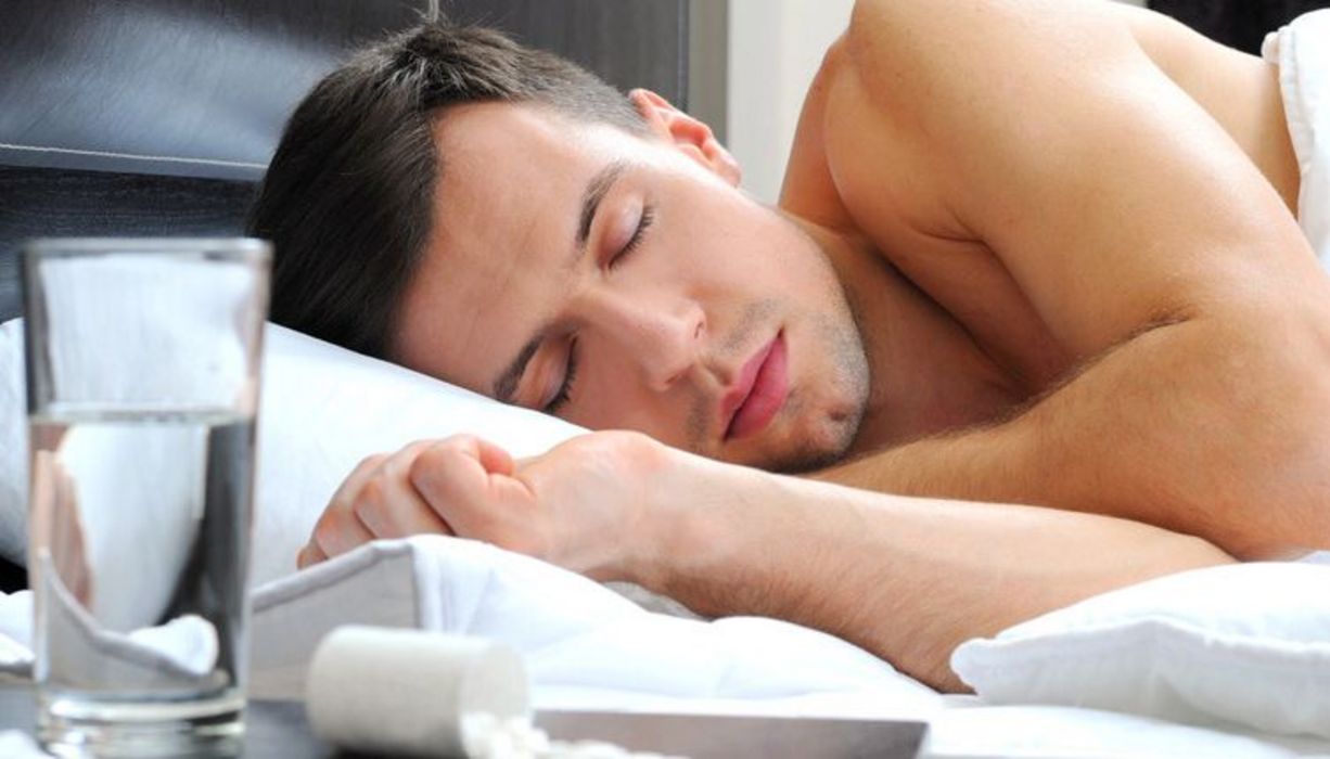 Junger, schlafender Mann; neben ihm auf dem Nachttischchen liegen Schlaftabletten