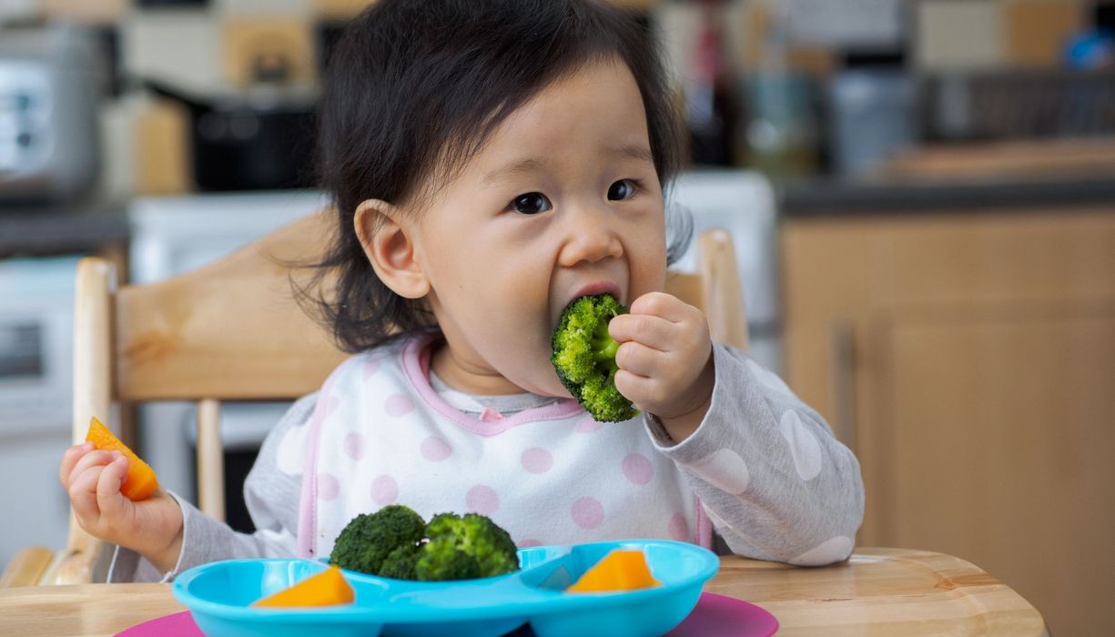 Kleinkind, isst Brokkoli und Kürbis.