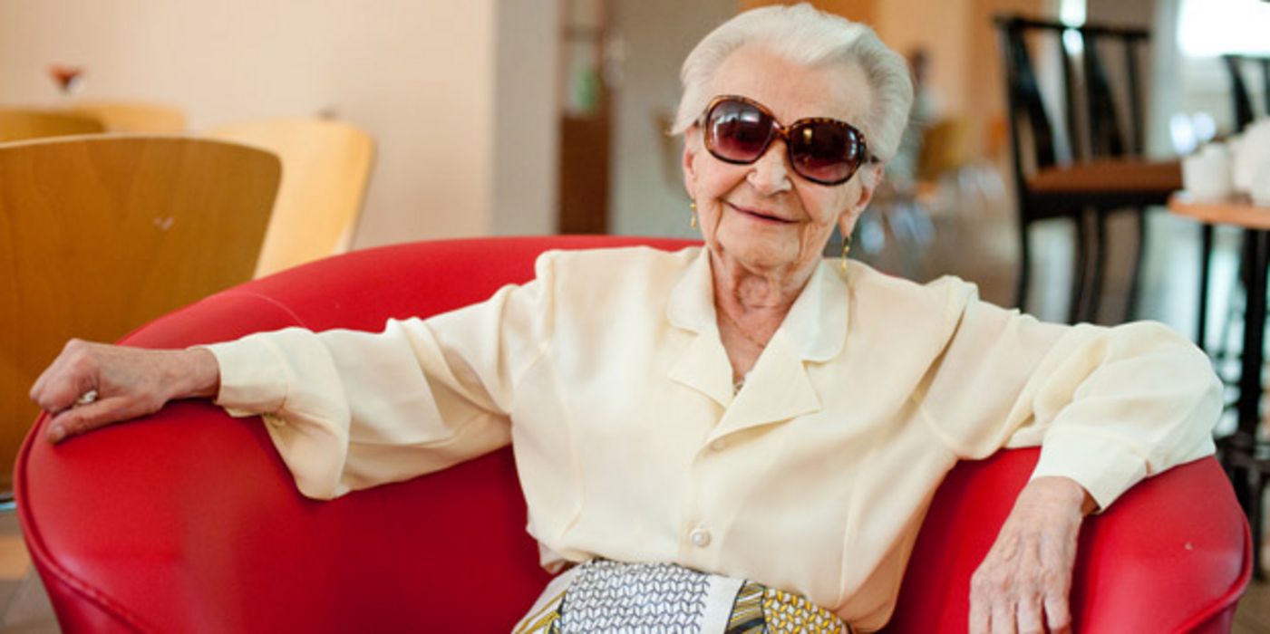 Ältere Frau mit Sonnenbrille sitzt auf einer Couch