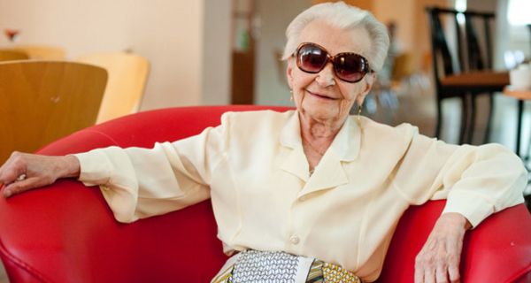 Ältere Frau mit Sonnenbrille sitzt auf einer Couch