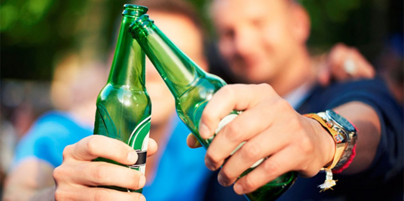 2 männliche Jugendliche, Hintergrund, unscharf, prosten sich zu: Vordergrund 2 Bierflaschen