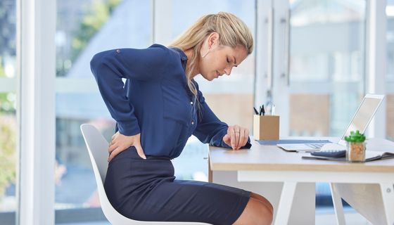Frau im Büro hält sich den Rücken.