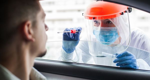 Frau mit Schutzkleidung, testet eine Person durch das Autofenster.