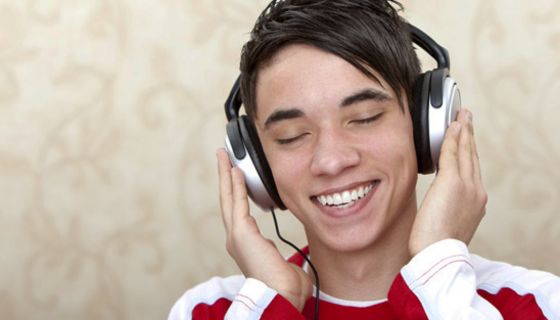 Junger Mann hört strahlend lächelnd über Kopfhörer Musik