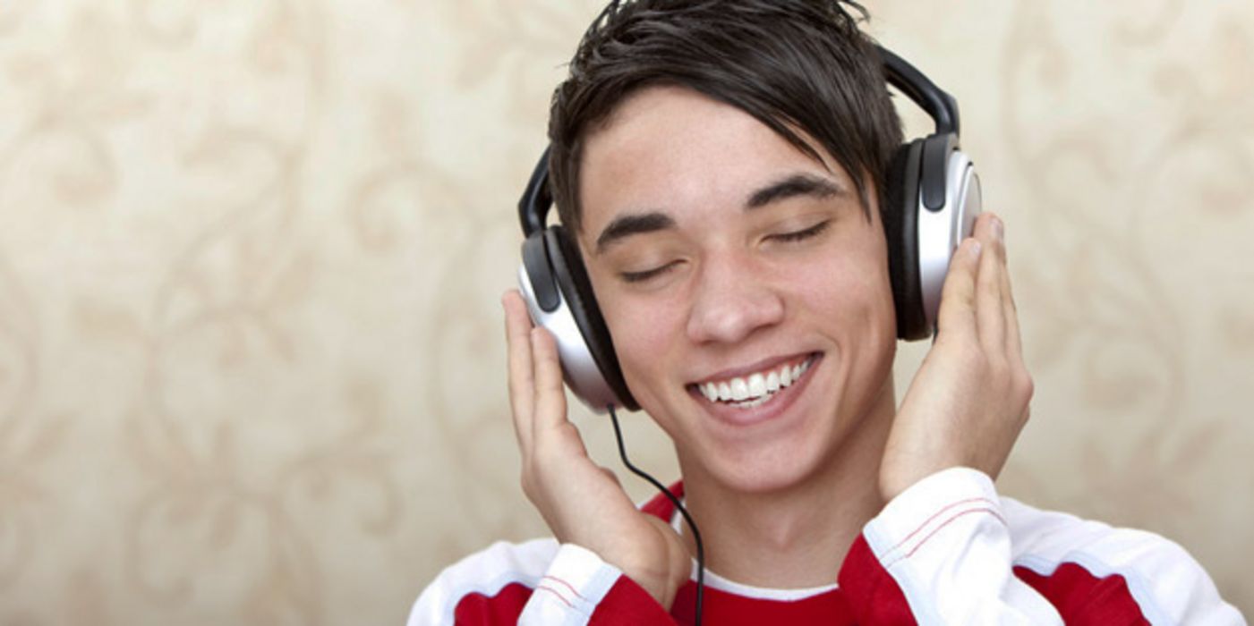 Junger Mann hört strahlend lächelnd über Kopfhörer Musik