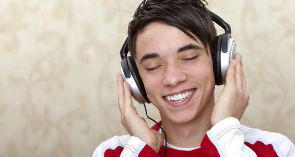 Junger Mann hört strahlend lächelnd über Kopfhörer Musik