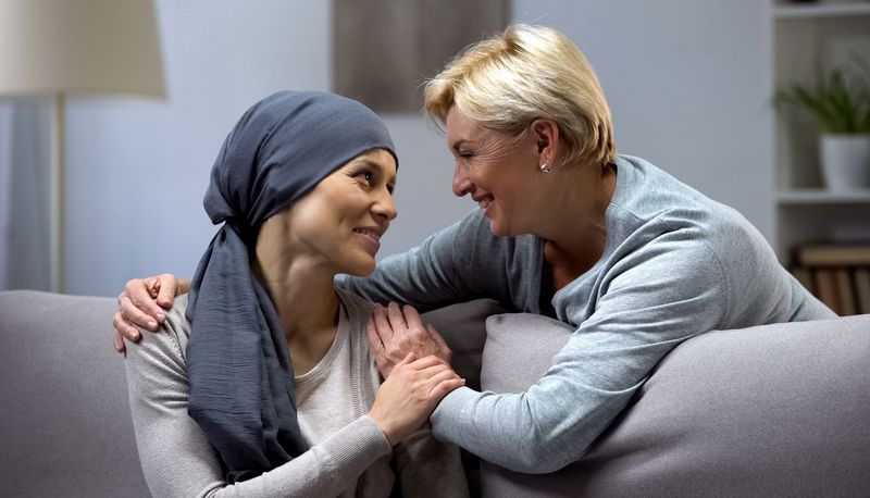 Krebspatientin, wird von hinten von einer älteren Frau umarmt, beide lächeln.