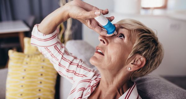 Frau, tropft sich Augentropfen in das Auge.